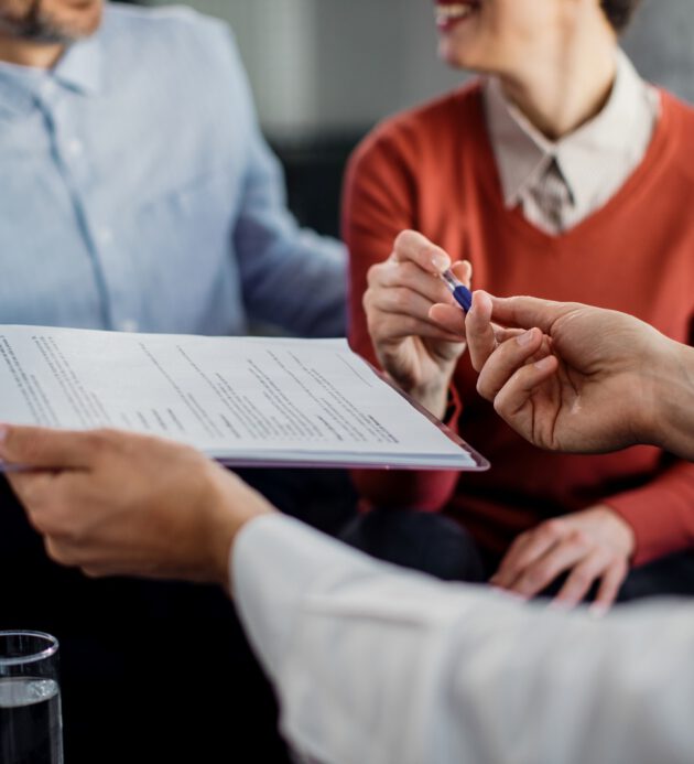 Close-up of unrecognizable couple signing a contract with financ Close-up of woman signing an agreement with insurance agent while being on a meeting with her husband.