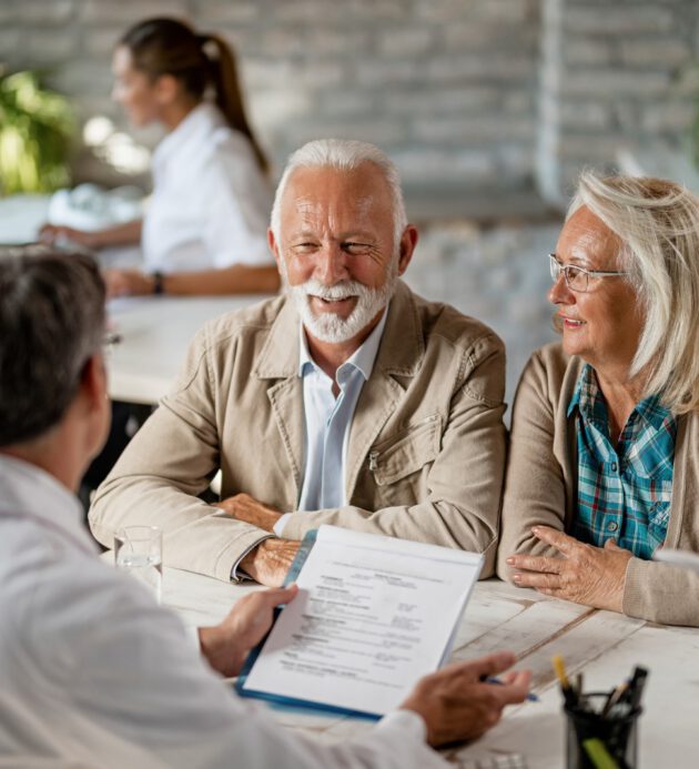 Happy mature couple talking to a doctor while going through their medical reports. Happy senior couple communicating with a doctor about their health insurance while going through paperwork.